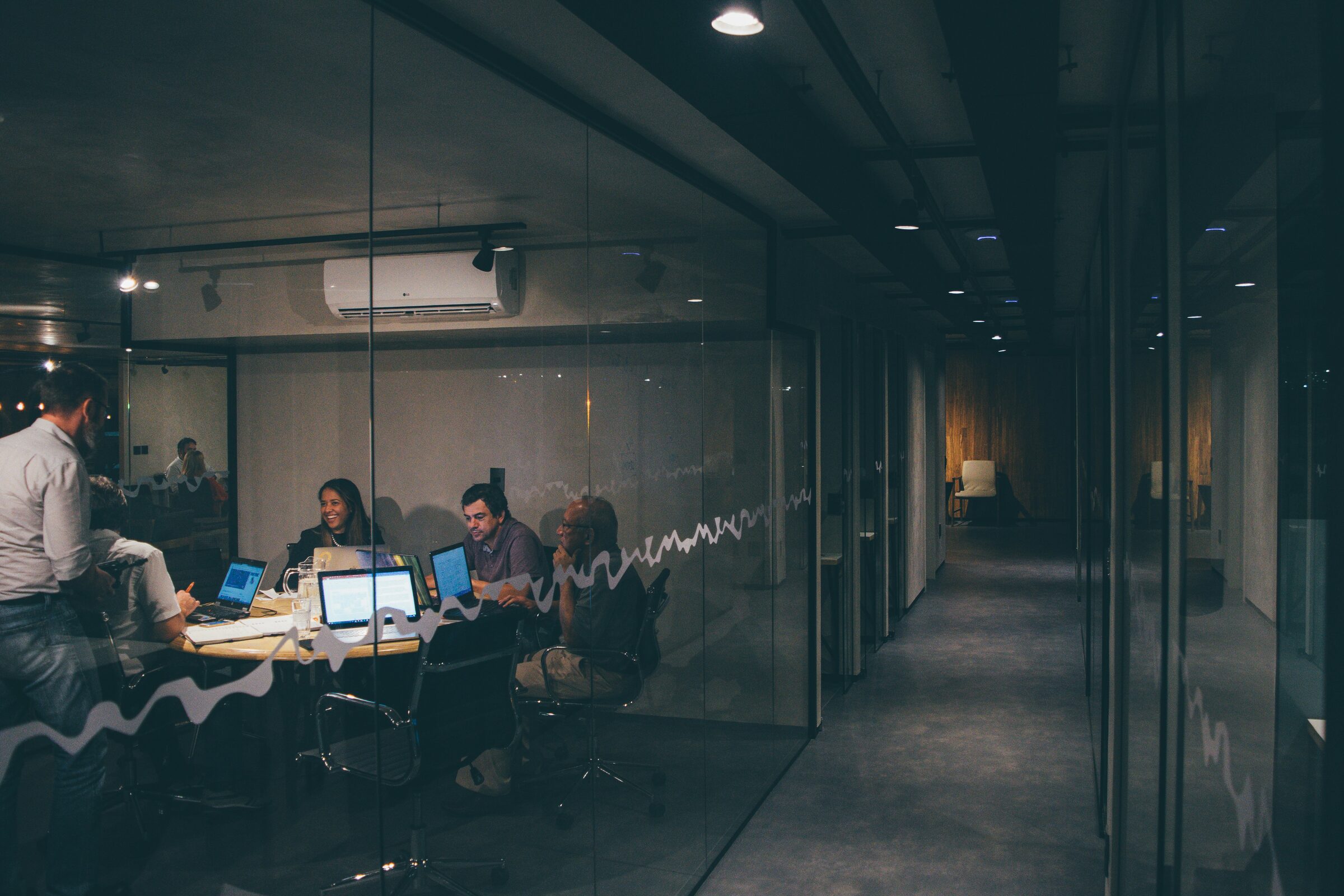 A team working on laptops in a glass-walled meeting room at night