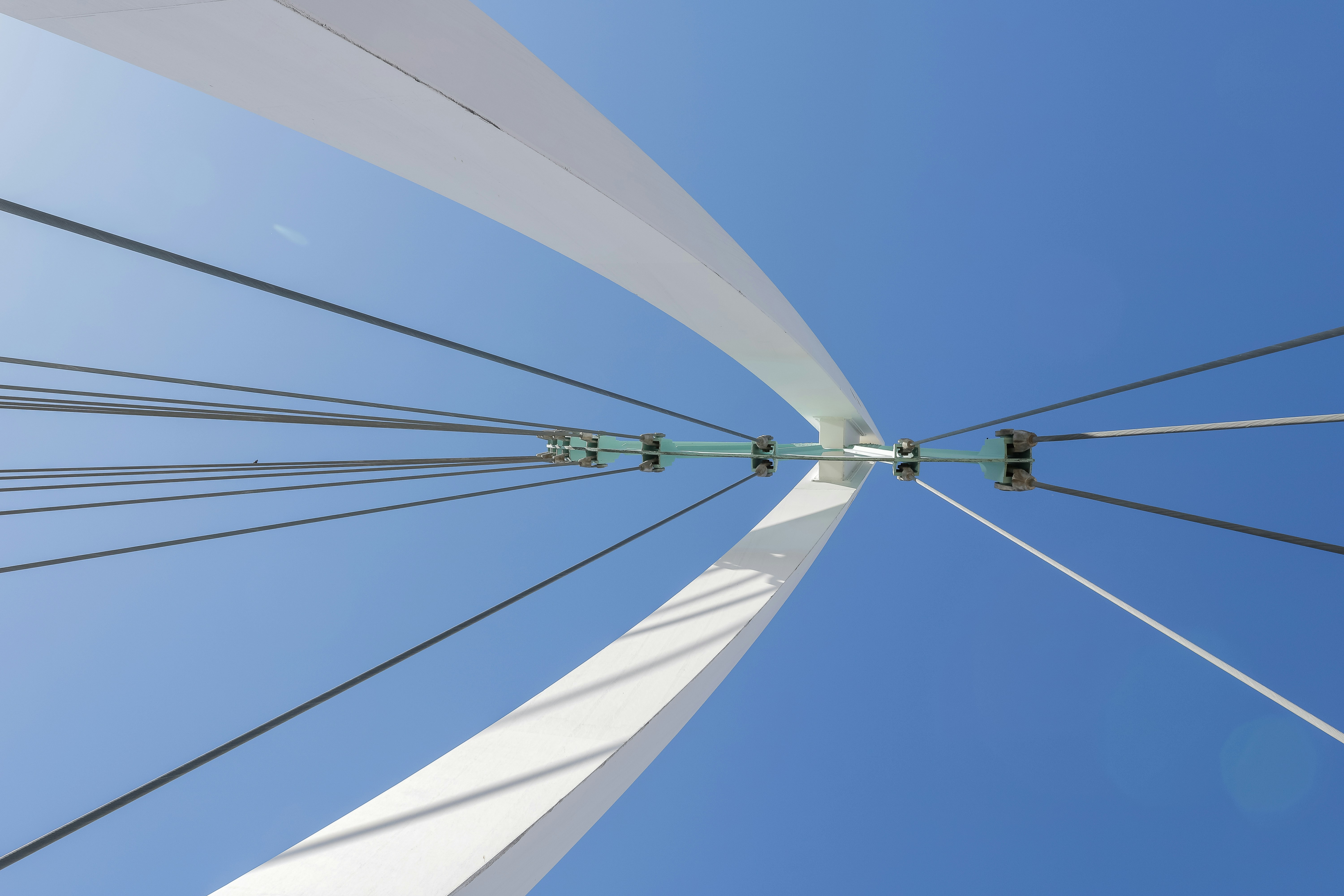 Looking up at a white bridge pylon and its converging steel cables